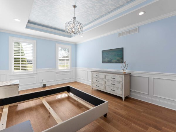 Modern bedroom in Bucks County, PA with light blue walls and white wainscoting, two windows and recessed lighting.