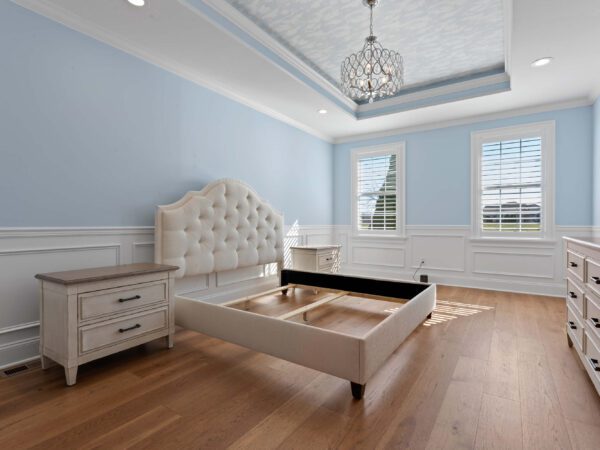 Modern bedroom in Bucks County, PA with light blue walls and white wainscoting, two windows and chandelier.