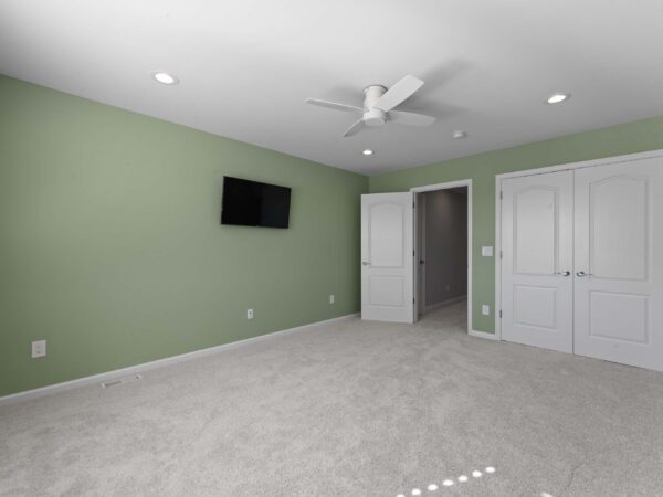 Modern bedroom in Bucks County, PA with light green walls, white door, and white ceiling fan.