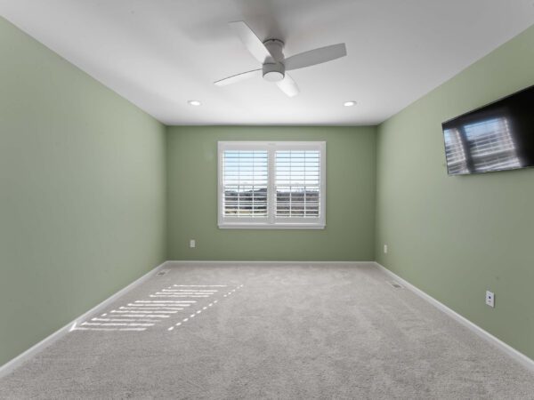 Modern bedroom in Bucks County, PA with light green walls, mounted TV, and window with white trim.