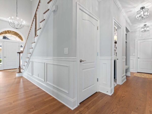 Modern hallway in Bucks County, PA with light grey walls, wood floors, white doors, and chandelier lights.