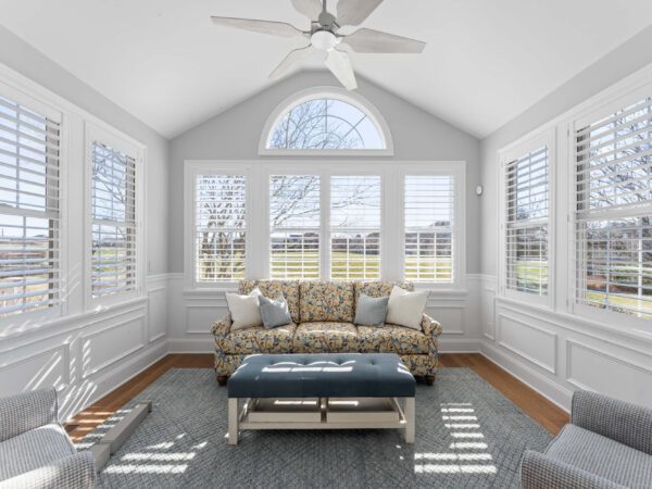 Modern sitting room in Bucks County, PA with light grey walls, vaulted ceiling, several windows, and wood floor with couch and chairs.