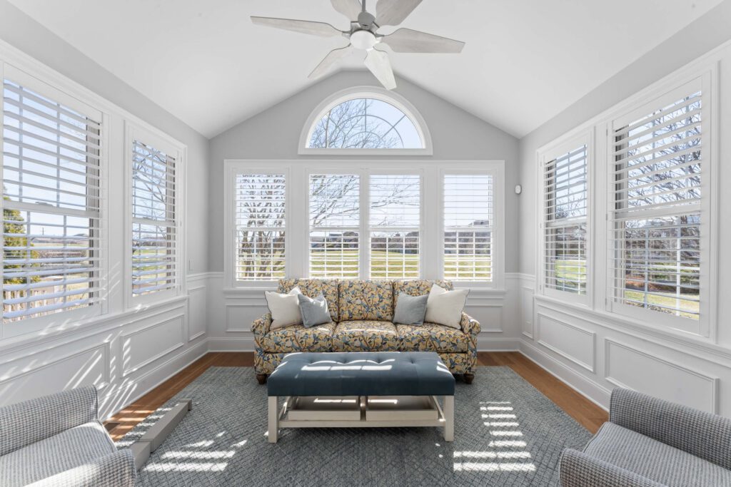Modern sitting room in Montgomery County, PA with light grey walls, vaulted ceiling, several windows, and wood floor with couch and chairs.