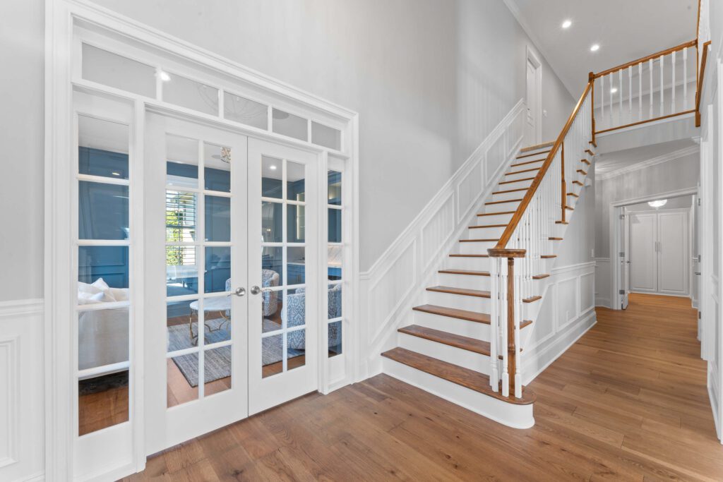 Modern stairway and hallway in Montgomery County, PA with light grey walls, wood steps and railing, and white trim.