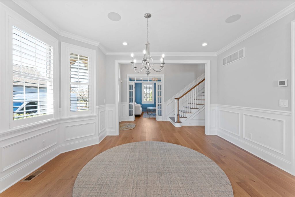 Modern entryway in Bucks County, PA with light grey walls, wood floors, area rugs, and chandelier.