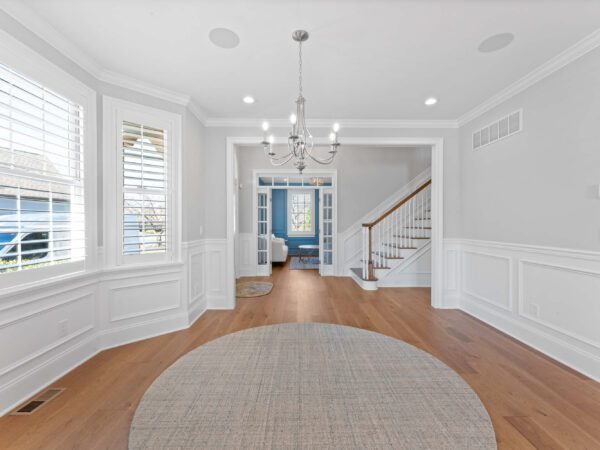 Modern entryway in Bucks County, PA with light grey walls, wood floors, area rugs, and chandelier.