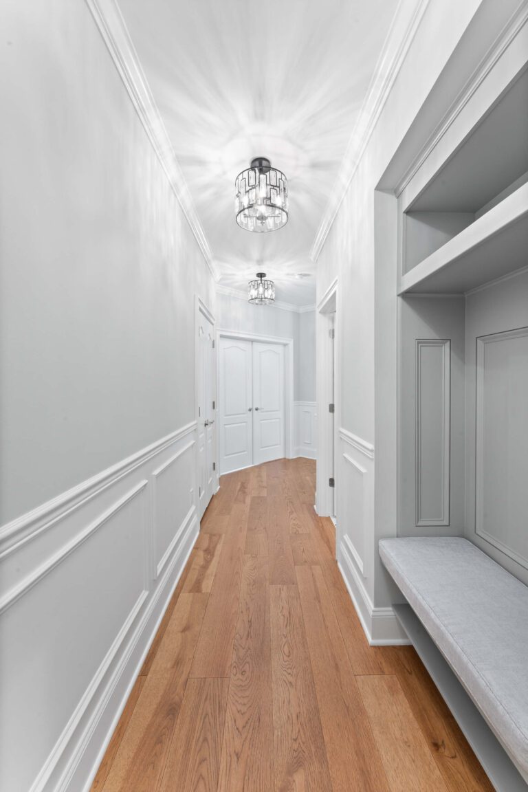 Modern hallway in Bucks County, PA with light grey walls, white wainscoting, wood floors, and chandelier.