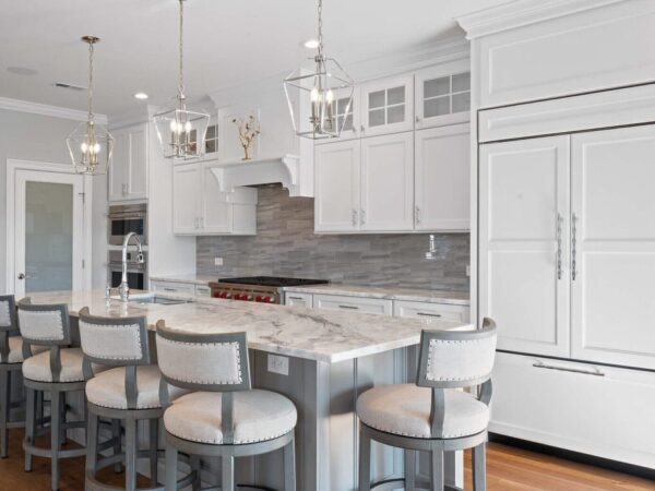 Modern kitchen in Bucks County, PA with white cabinets, grey backsplash, marble countertops, island with chairs, and recessed lighting.