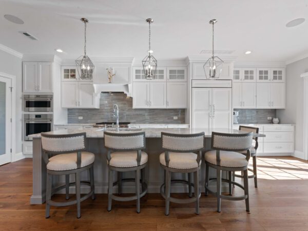 Modern kitchen in Bucks County, PA with white cabinets, wood floors, white ceiling, marble countertops, and island with chairs.