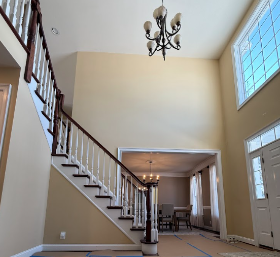 Two-story foyer with beige walls, staircase, chandelier, and adjacent dining room with large windows.