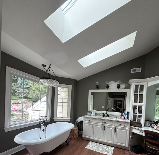 Bathroom with freestanding tub, skylights, large window, and white vanity with mirror.
