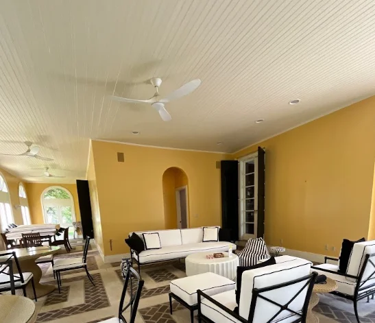 Spacious room with yellow walls, white ceiling, modern furniture, ceiling fans, and large windows.