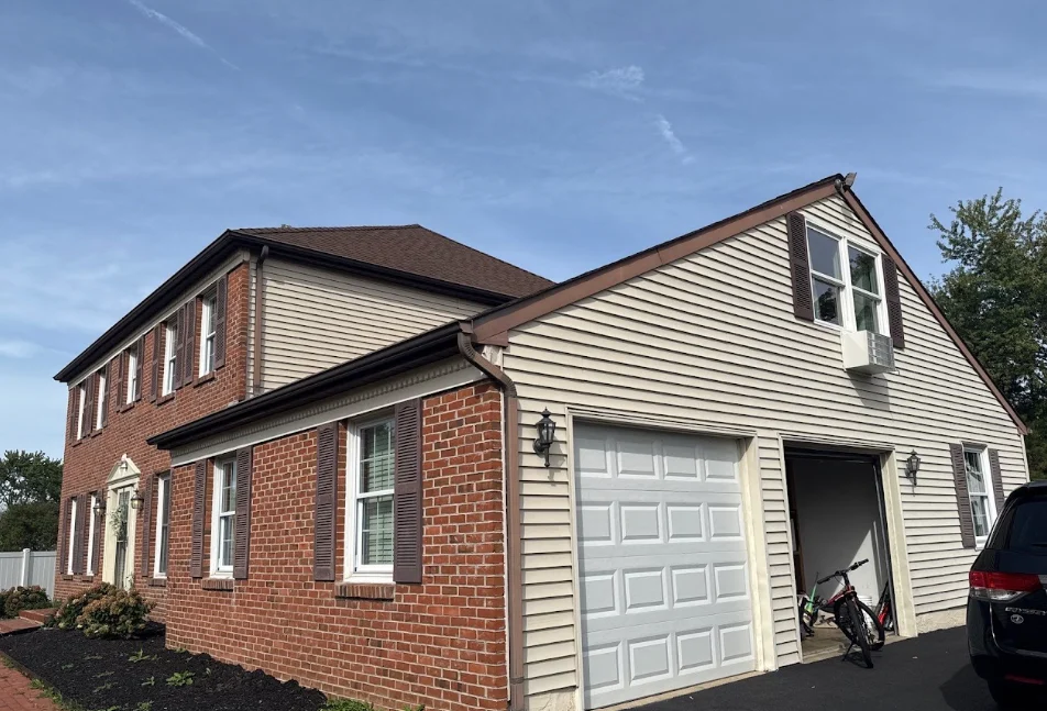 Two-story house with brick and siding exterior, garage door open, bicycle inside, car parked outside, clear sky.